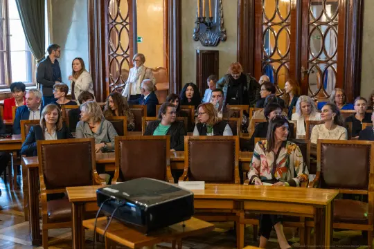 Grupa osób siedzących w sali konferencyjnej, przygotowujących się do spotkania.