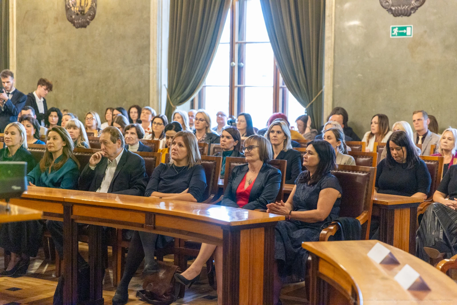 Grupa ludzi siedzących w sali podczas wydarzenia, z widocznymi stołami i oknami.  Autor: Bogusław Świerzowski