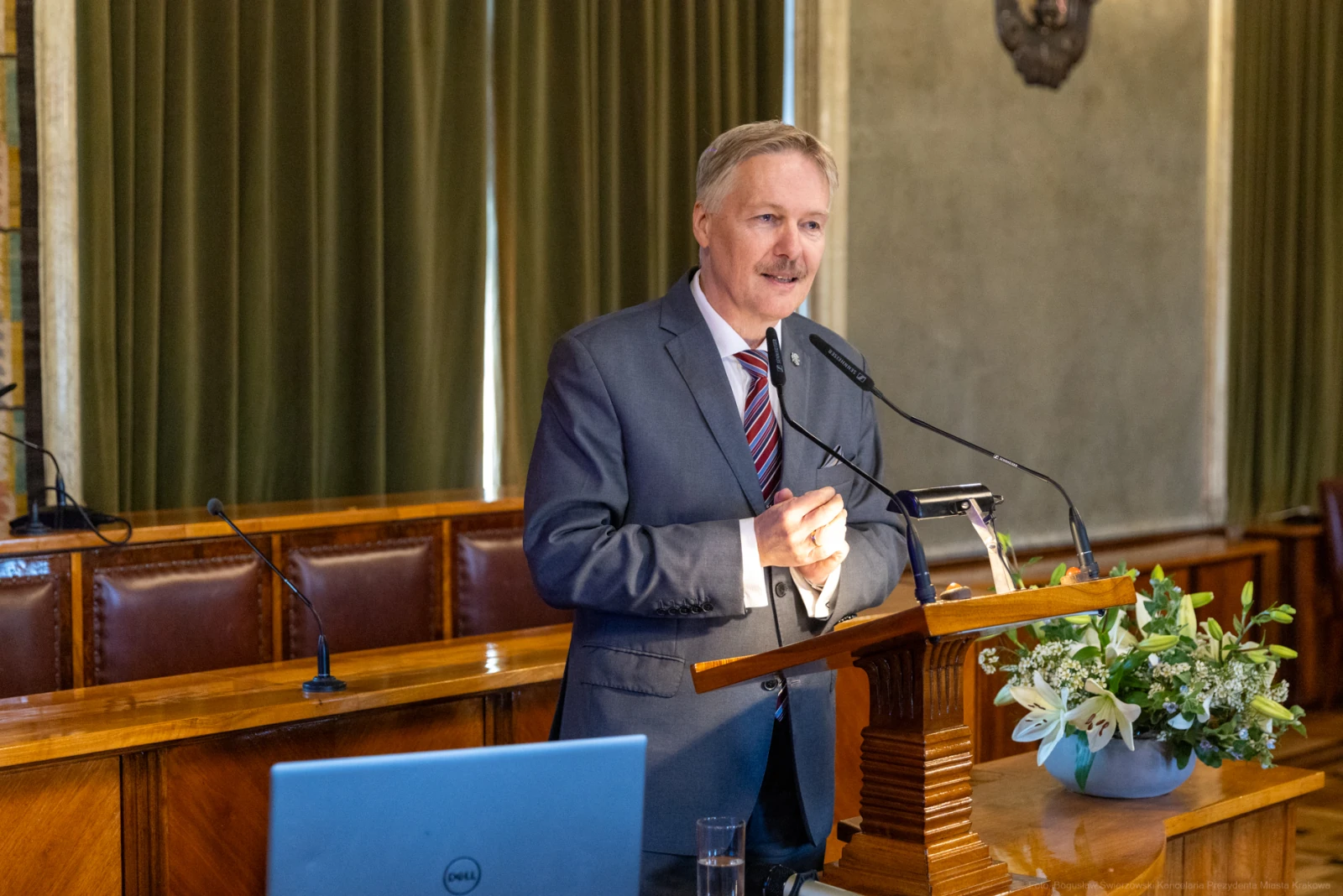 Mężczyzna w garniturze przemawia z mównicy, obok kwiaty i laptop.  Autor: Bogusław Świerzowski