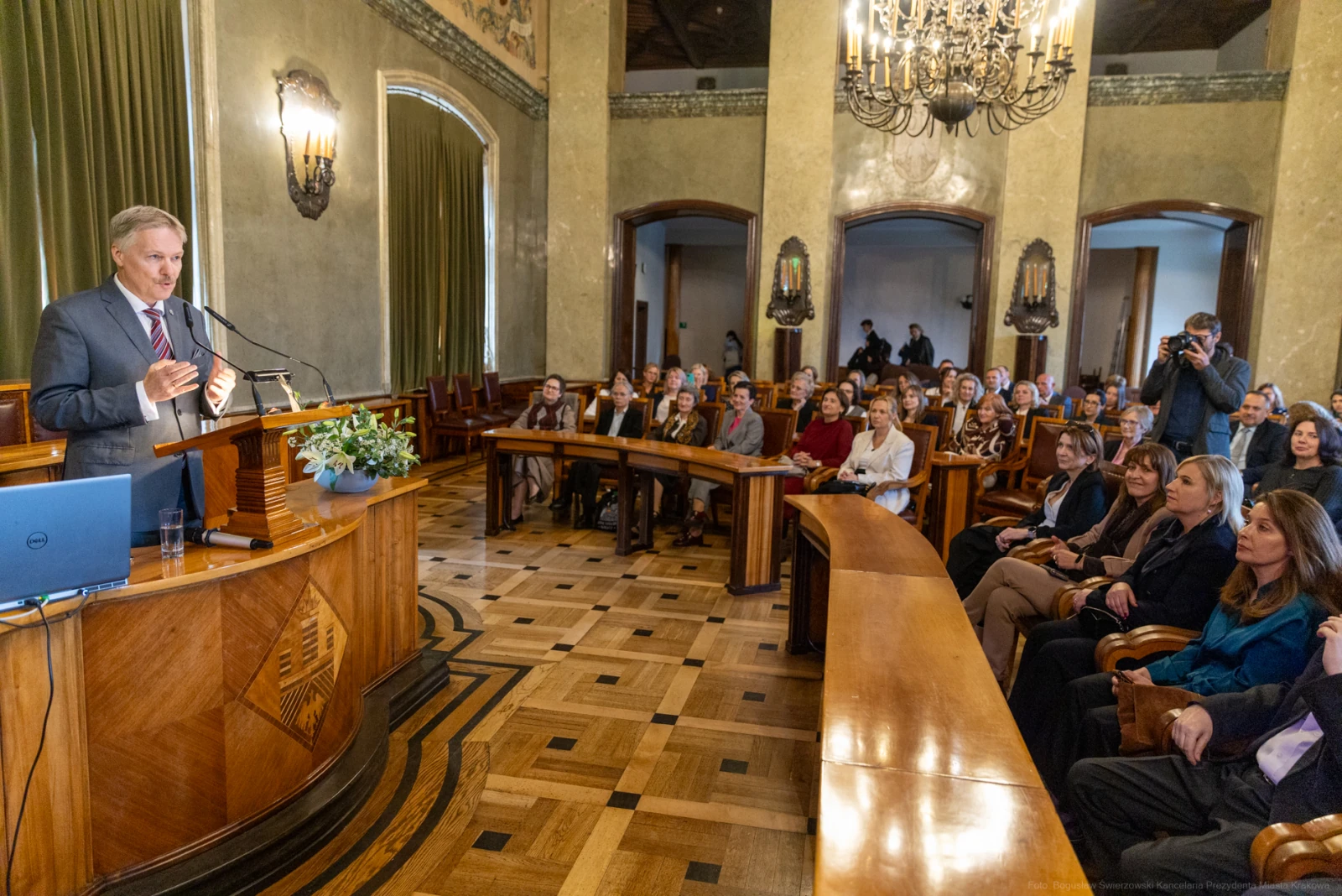 Mężczyzna przemawia do zgromadzonej publiczności w eleganckiej sali.  Autor: Bogusław Świerzowski