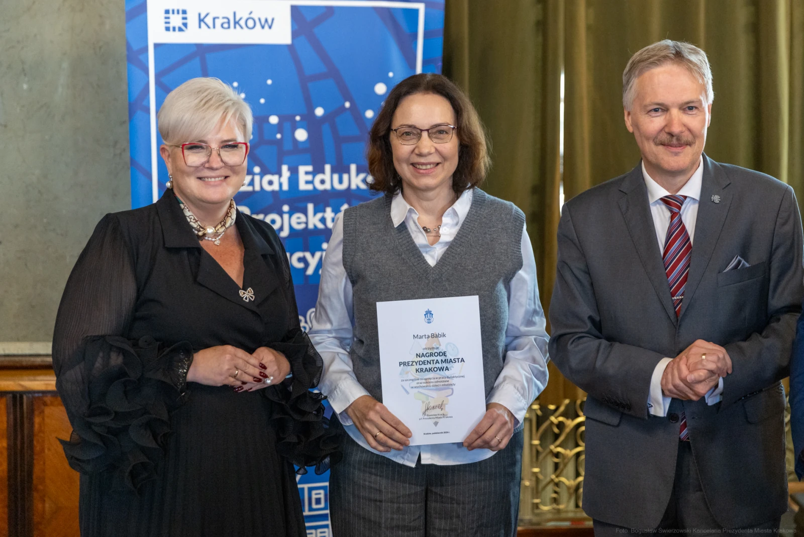 Trzy osoby pozujące z dyplomem w tle z logo Krakowa.  Autor: Bogusław Świerzowski