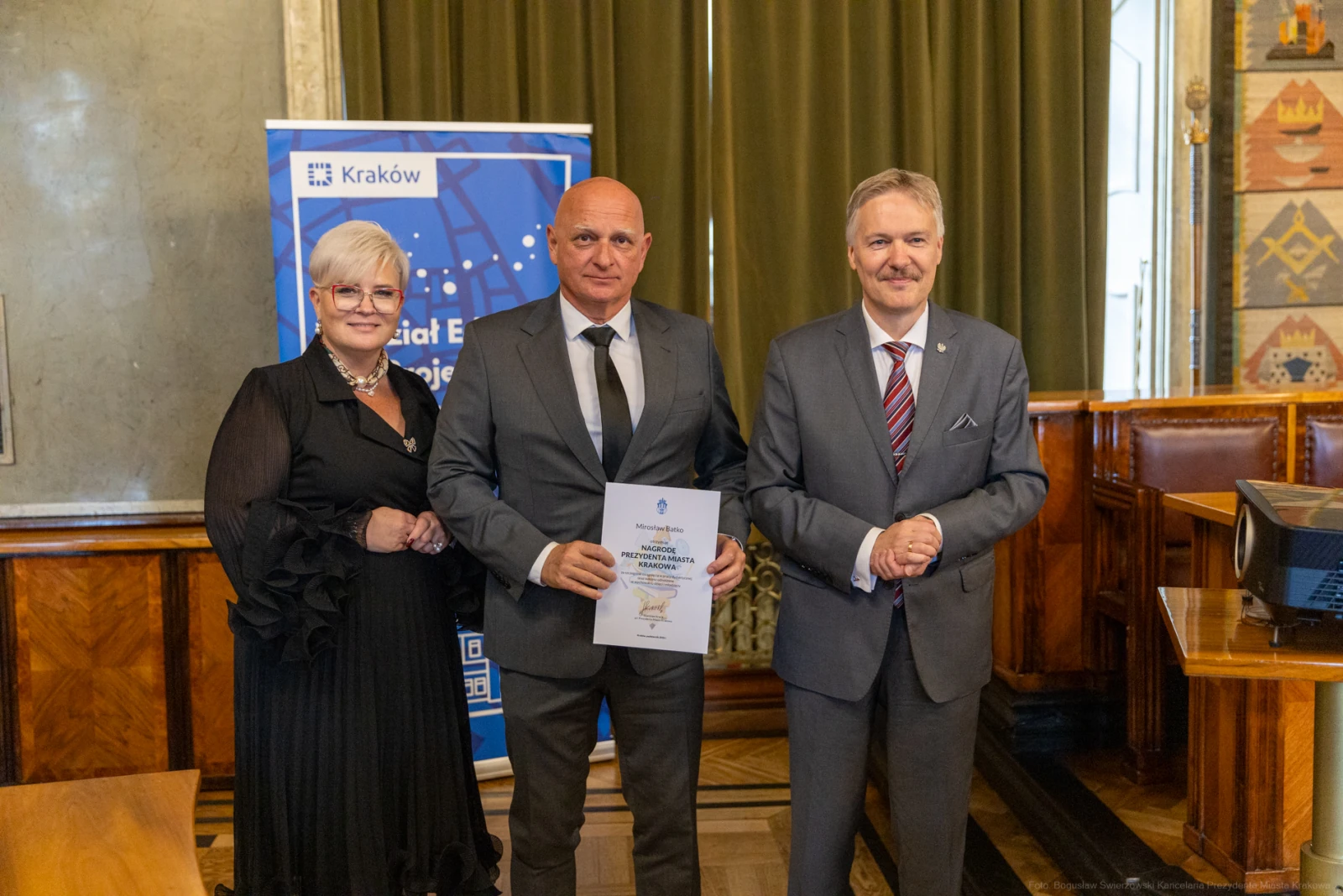Wręczenie nagrody w Krakowie, trzech osób w formalnych strojach, dokument w rękach jednego z uczestników.  Autor: Bogusław Świerzowski