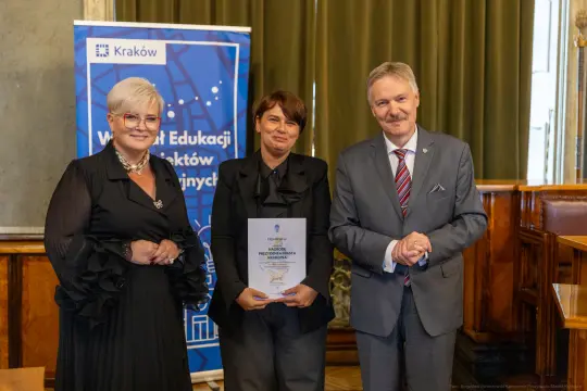 Wręczenie nagrody w Krakowie, trzy osoby w formalnych strojach, dokument w rękach jednej z nich.