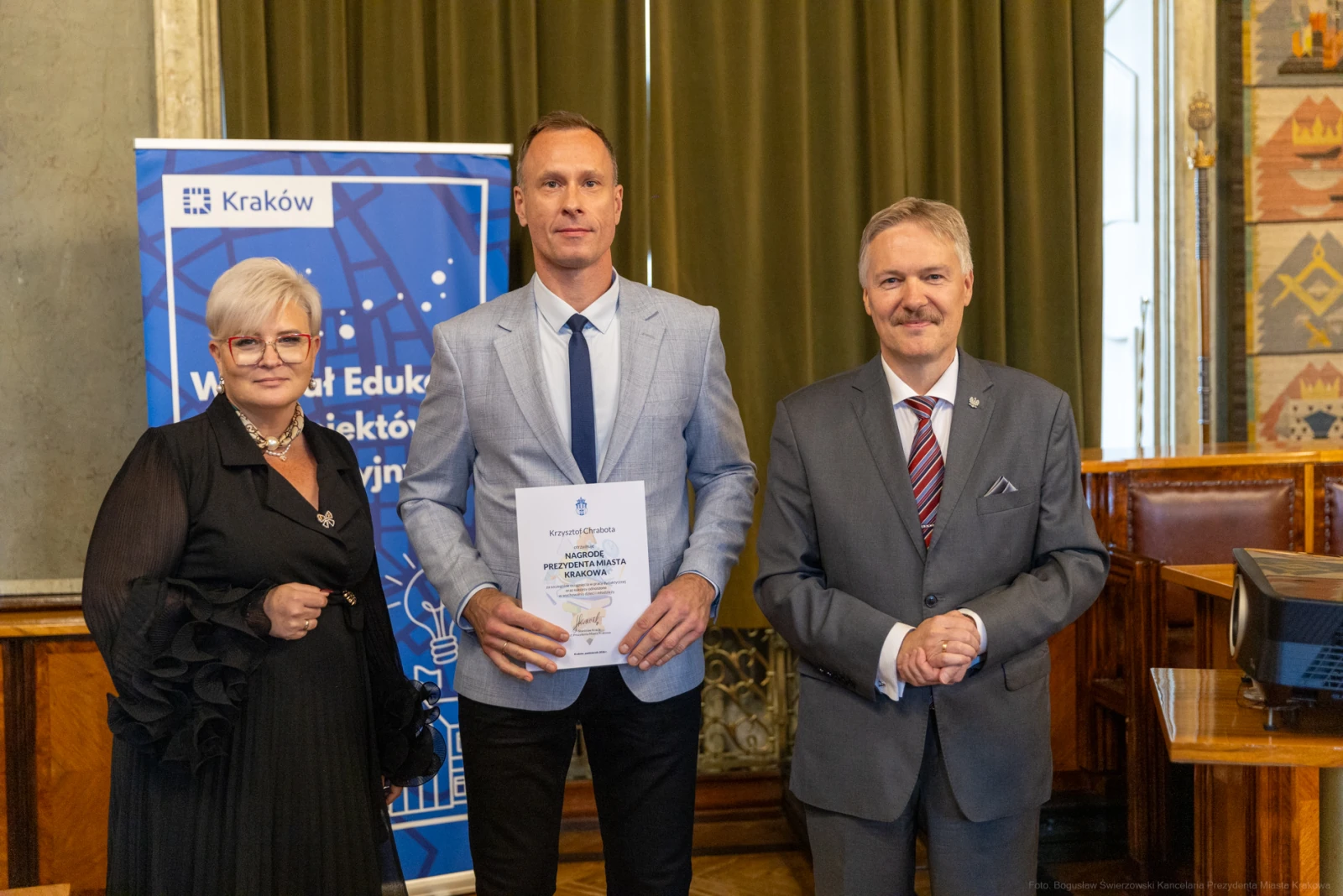 Trzy osoby w formalnych strojach trzymają dyplom w sali z dekoracjami.  Autor: Bogusław Świerzowski