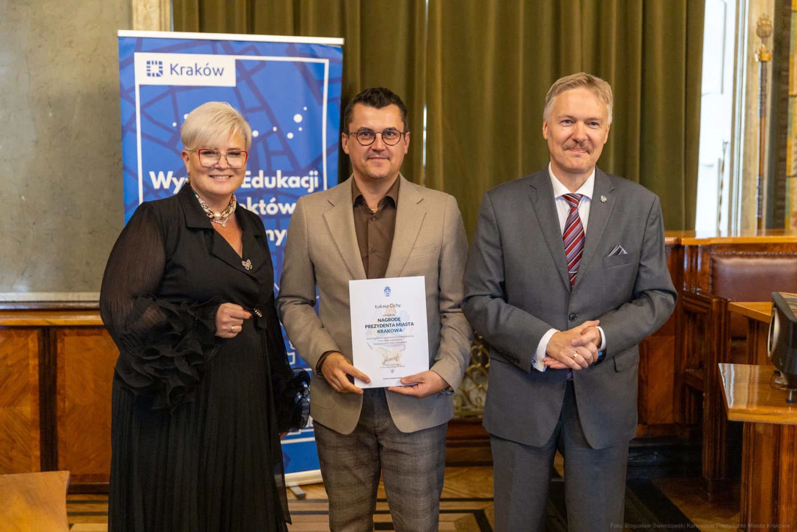Trzech mężczyzn i kobiet w formalnych strojach, trzymających dyplom w sali z eleganckim wystrojem.  Autor: Bogusław Świerzowski