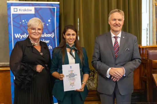 Trzy osoby pozujące z dyplomem w sali miejskiej w Krakowie.