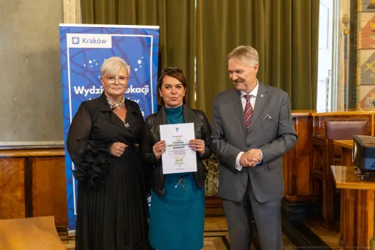Wręczenie dyplomu w Wydziale Edukacji w Krakowie. Trzy osoby w formalnych strojach.