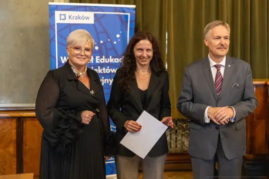 Trzy osoby w formalnych strojach podczas wydarzenia edukacyjnego w Krakowie.