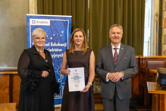 Wręczenie nagrody w Krakowie, trzy osoby pozujące z dyplomem.