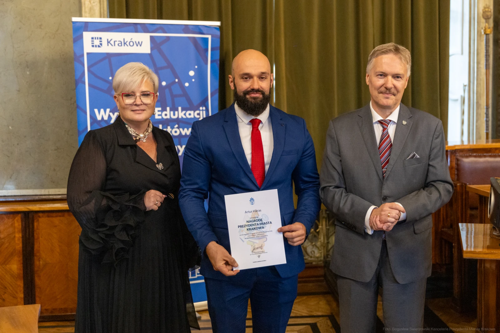 Wręczenie nagrody w Krakowie, trzech osób w formalnych strojach, dyplom w rękach mężczyzny.  Autor: Bogusław Świerzowski