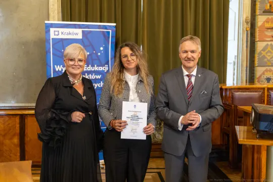 Wręczenie nagrody w Krakowie, trzy osoby pozujące z dyplomem.