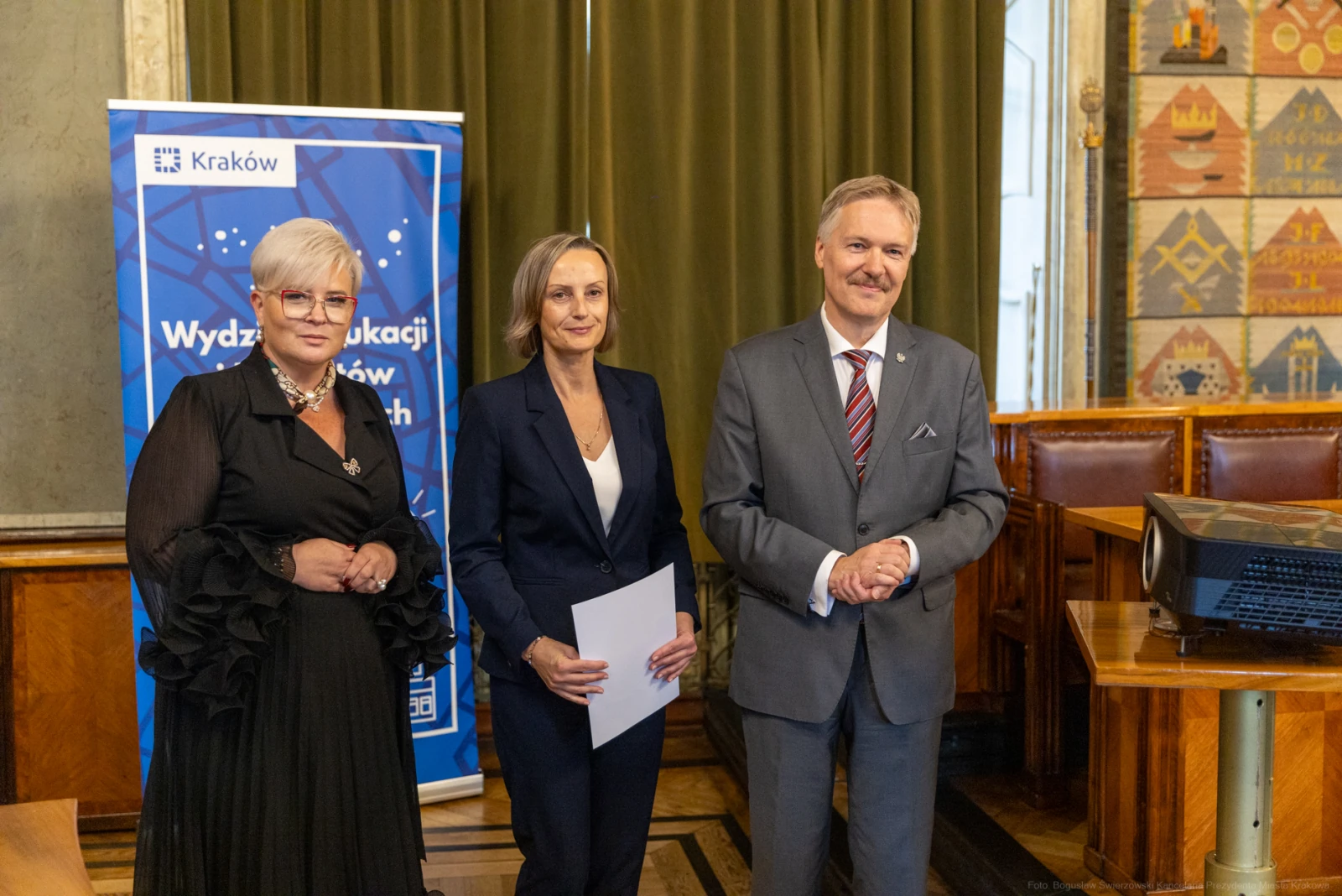 Trzy osoby w formalnych strojach stoją obok siebie w sali z dekoracjami.  Autor: Bogusław Świerzowski