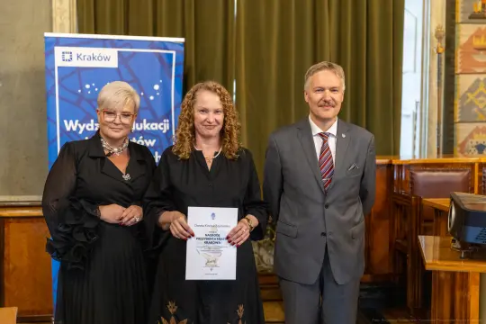 Wręczenie nagrody w Krakowie, trzy osoby pozujące z dyplomem.