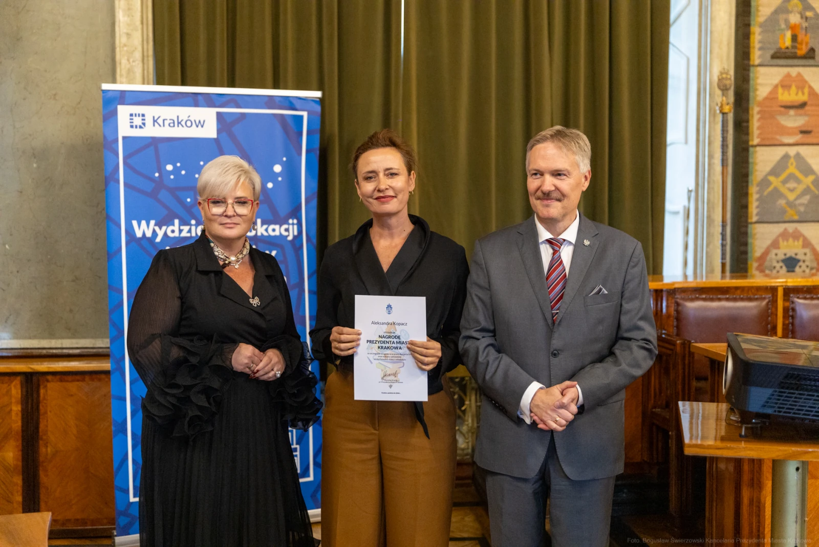 Trzy osoby w formalnych strojach trzymają dokument w sali konferencyjnej.  Autor: Bogusław Świerzowski