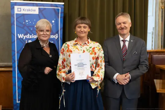 Trzy osoby stojące obok siebie, jedna z dyplomem, w tle baner z logo Krakowa.