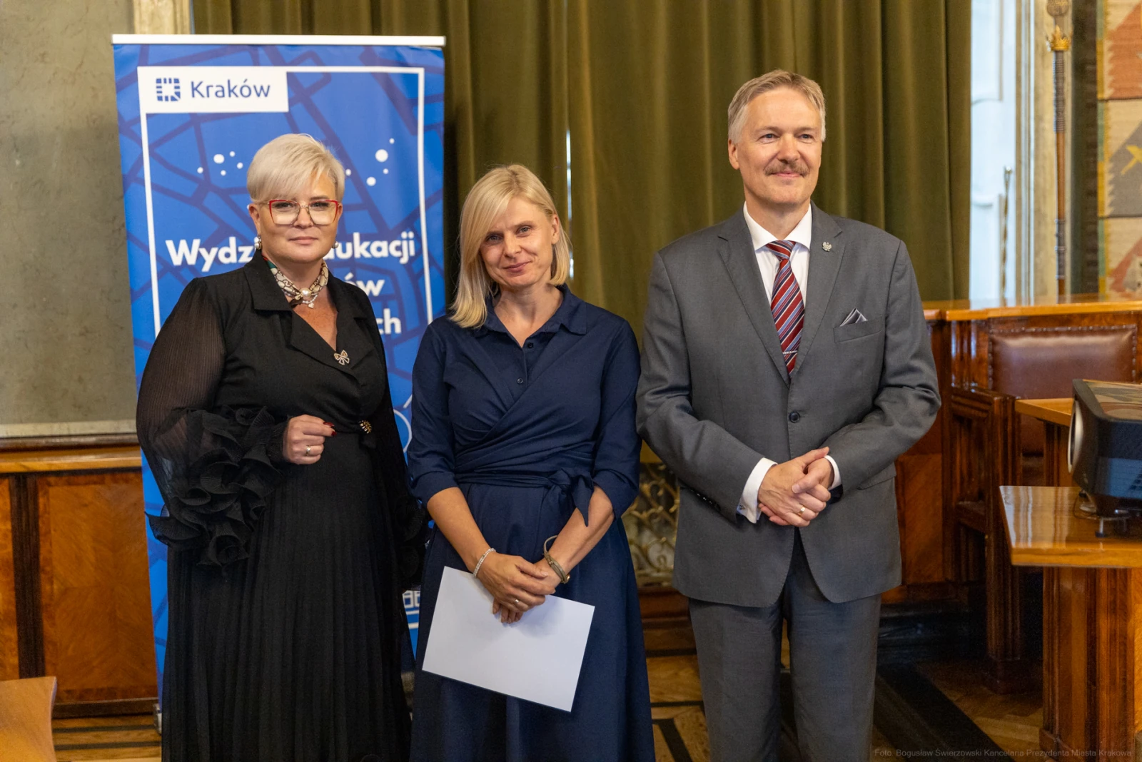 Trzy osoby w formalnych strojach, stojące obok siebie w sali z zielonymi zasłonami.  Autor: Bogusław Świerzowski