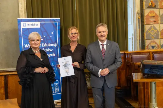 Wręczenie nagrody w dziedzinie edukacji w Krakowie. Trzy osoby w formalnych strojach.