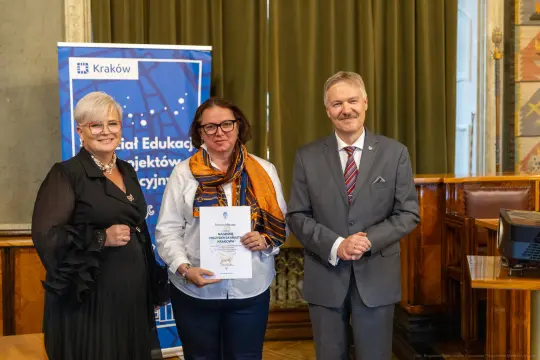 Wręczenie nagrody w Krakowie, trzy osoby w formalnych strojach, dokument w rękach jednej z nich.