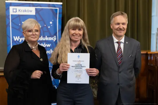 Kobieta trzymająca dyplom, obok dwóch osób w formalnych strojach. Tło z logo Krakowa.