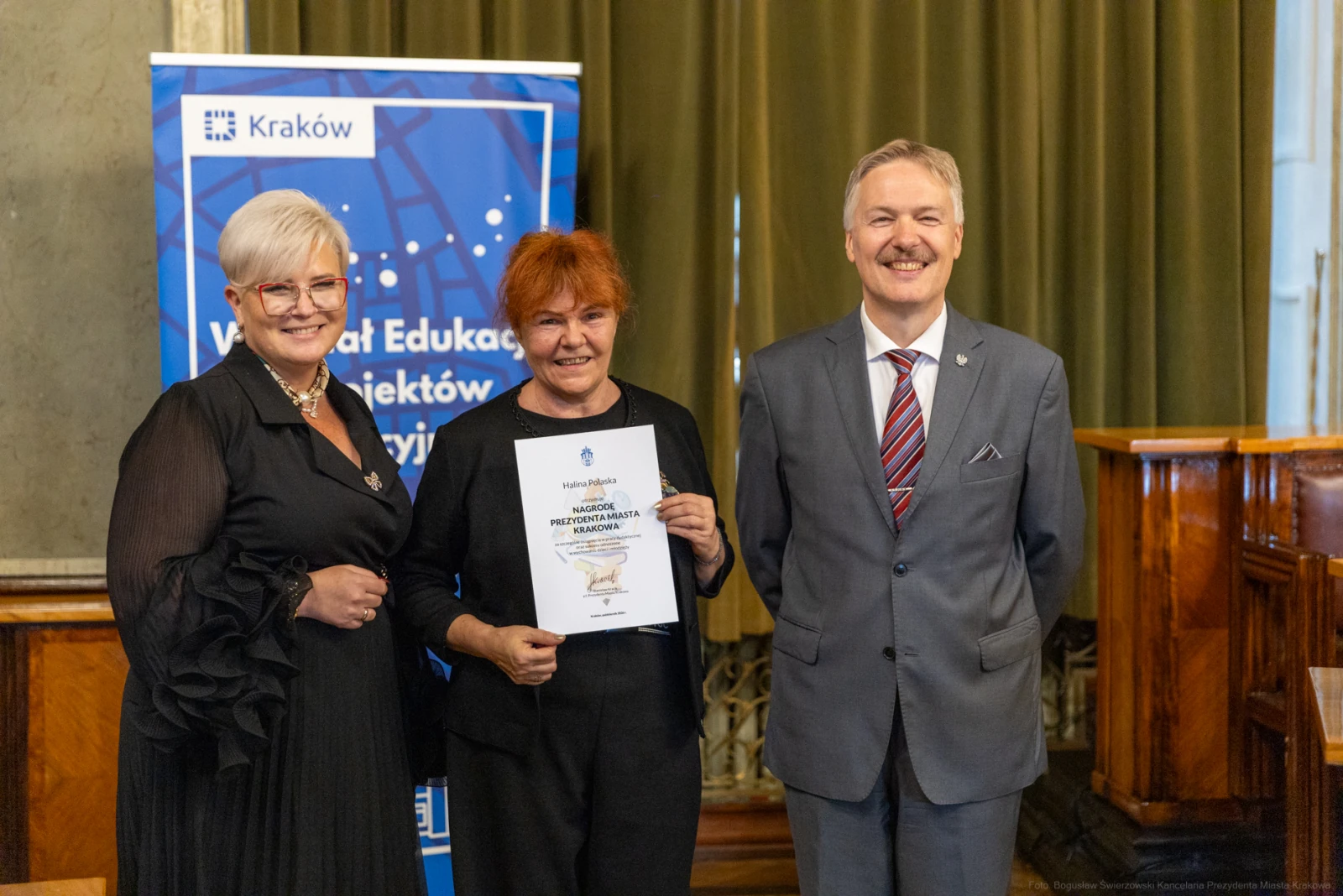 Trzy osoby w formalnych strojach trzymają dyplom w sali z dekoracjami.  Autor: Bogusław Świerzowski