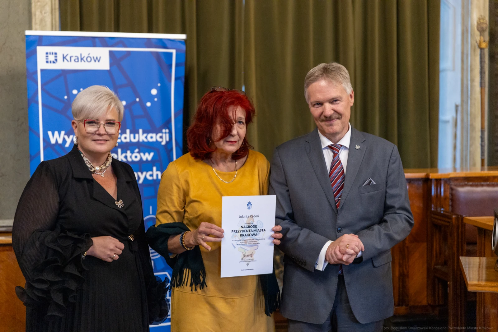 Trzy osoby w formalnych strojach trzymają dyplom w sali z dekoracjami.  Autor: Bogusław Świerzowski