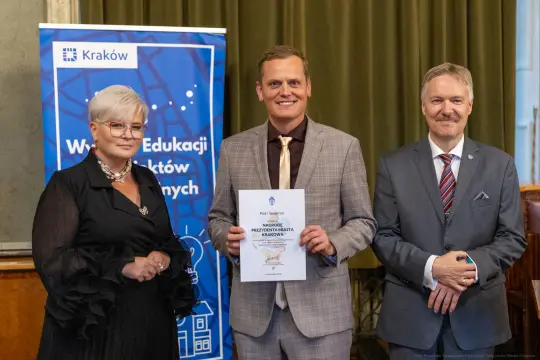 Uroczystość wręczenia nagrody w Krakowie, trzej mężczyźni i kobieta z dokumentem.