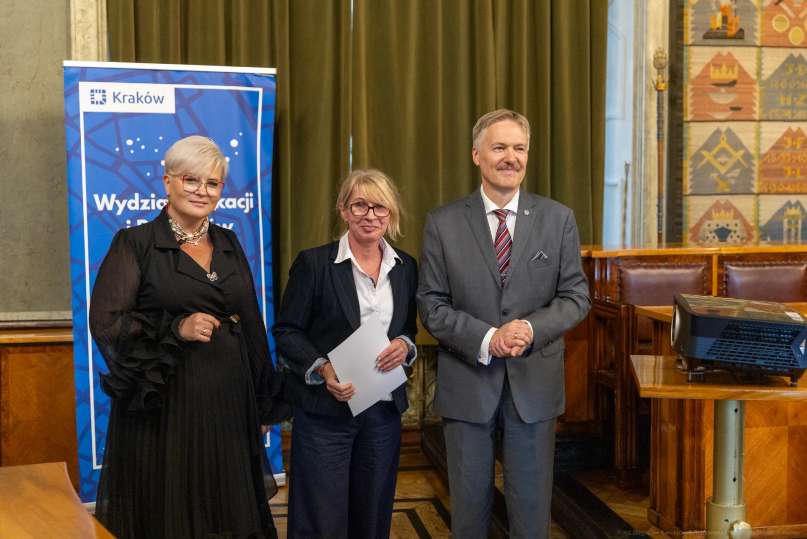 Trzy osoby w formalnych strojach stoją obok siebie w sali z dekoracjami.  Autor: Bogusław Świerzowski