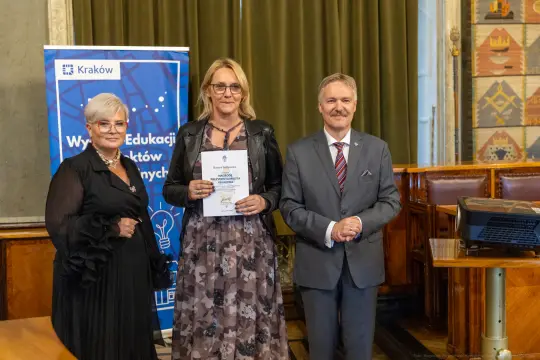 Wręczenie nagrody w Krakowie, trzy osoby pozujące z dyplomem.