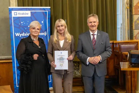 Wręczenie nagrody w Krakowie, trzy osoby pozujące z dyplomem.