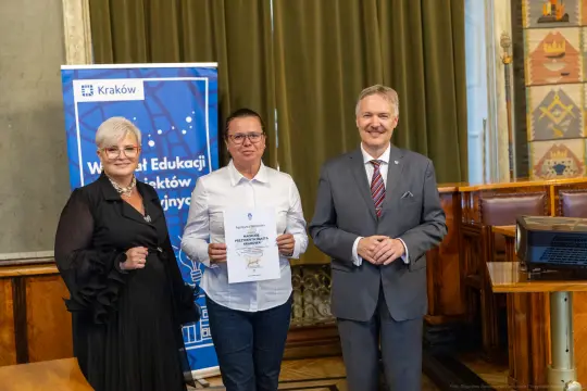 Wręczenie nagrody w Krakowie, kobieta z dyplomem, dwóch mężczyzn obok.