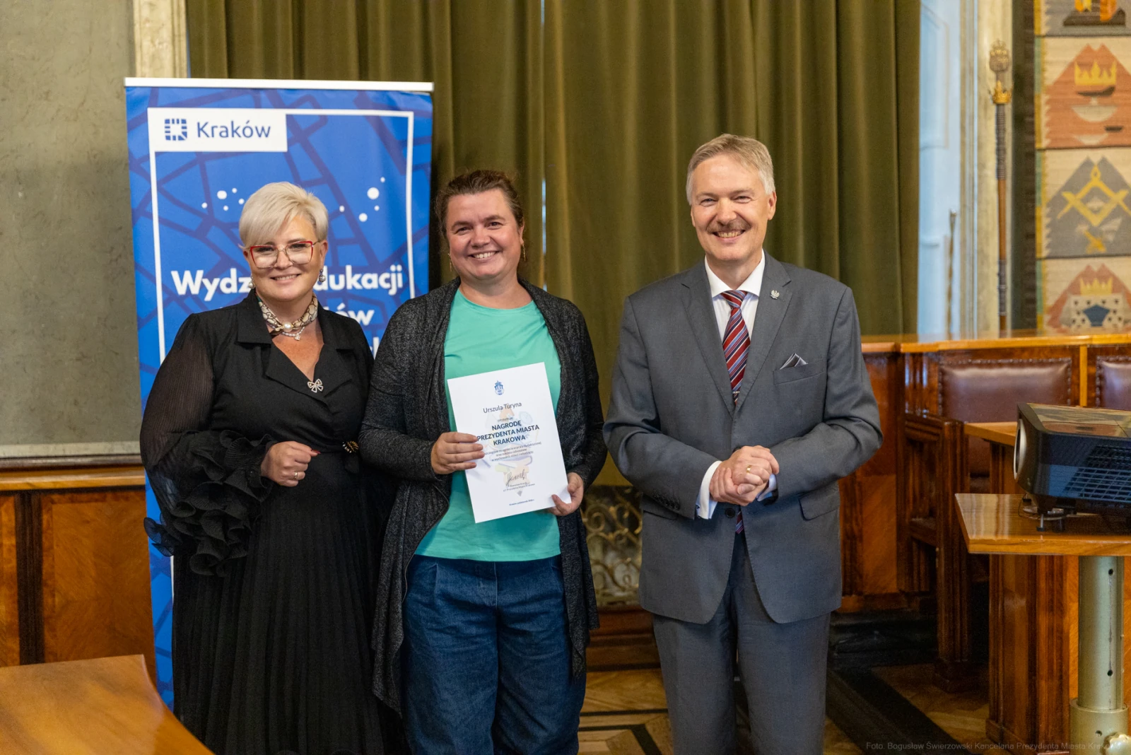 Wręczenie dyplomu w sali miejskiej, uśmiechnięte osoby w formalnych strojach.  Autor: Bogusław Świerzowski