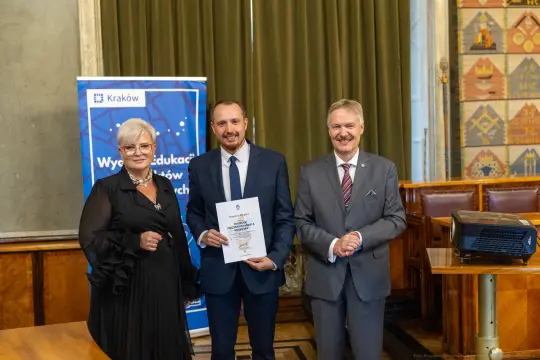 Wręczenie dyplomu w Krakowie, trzej mężczyźni w formalnych strojach, jeden z dyplomem w ręku.