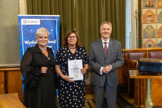 Wręczenie nagrody w Wydziale Edukacji w Krakowie. Trzy osoby pozujące z dyplomem.