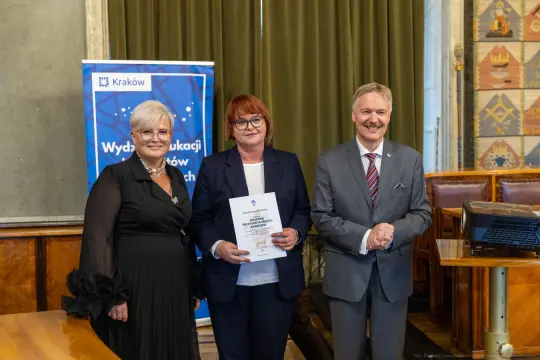 Wręczenie nagrody w Krakowie, trzy osoby pozujące z dyplomem.