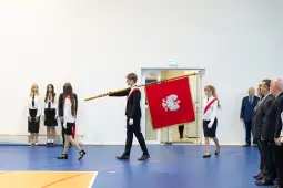 Uroczystość z pocztem sztandarowym, młodzież w strojach galowych, flagi i goście.