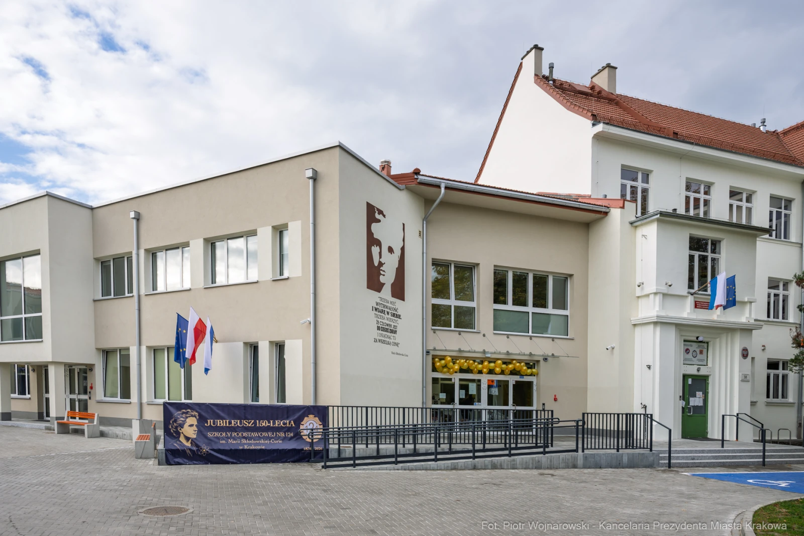 Budynek szkoły z flagami i tablicą pamiątkową na elewacji.  Autor: Piotr Wojnarowski