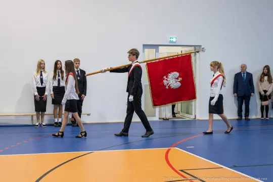 Uroczystość z pocztem sztandarowym i uczestnikami w strojach galowych.