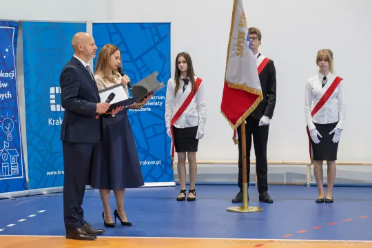 Uroczystość z przemówieniem, sztandar i osoby w mundurach.