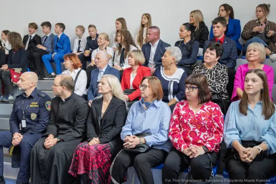 Grupa ludzi w różnych strojach siedzących na widowni, wśród nich dzieci i dorośli.