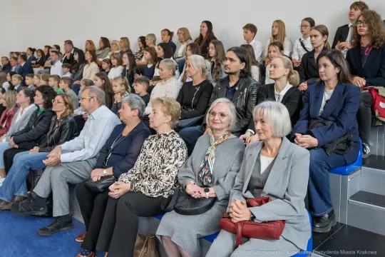 Grupa ludzi siedzących na widowni, różne pokolenia, w różnorodnych strojach.