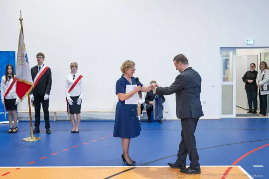 Wręczenie nagrody w sali gimnastycznej, uczestnicy w strojach galowych.
