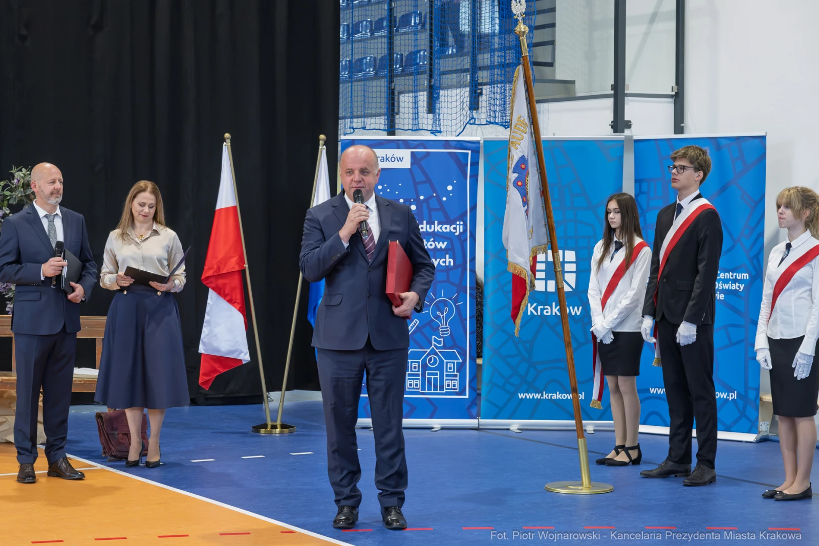 Uroczystość wręczenia nagród w szkole, przemówienie dyrektora, obecność uczniów z flagami.  Autor: Piotr Wojnarowski