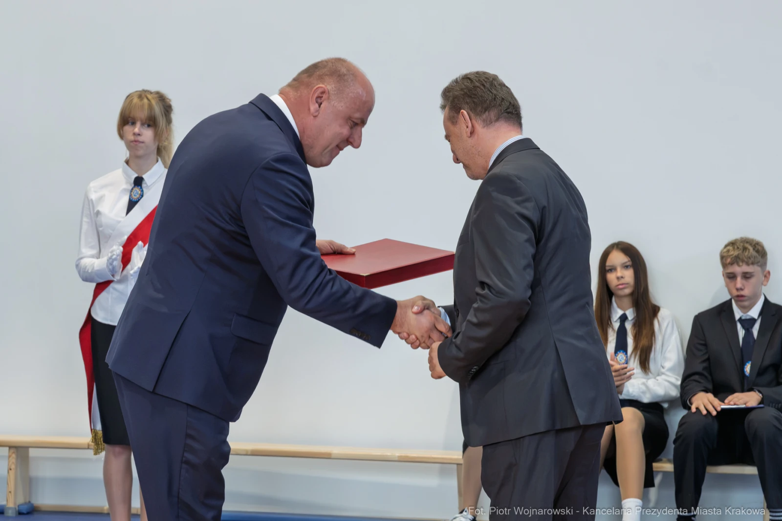 Wręczenie dyplomu podczas uroczystości szkolnej z udziałem uczniów i nauczycieli.  Autor: Piotr Wojnarowski