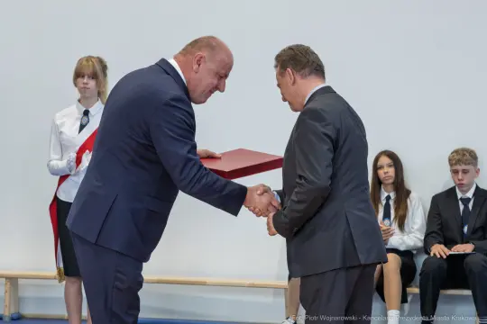 Wręczenie dyplomu podczas uroczystości szkolnej z udziałem uczniów i nauczycieli.