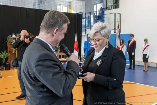 Wręczenie odznaczenia podczas uroczystości w hali sportowej.