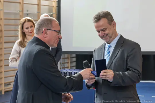Wręczenie nagrody przez mężczyznę w garniturze, obok uśmiechająca się kobieta.