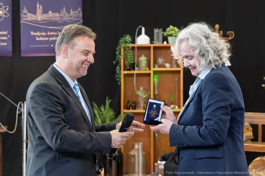 Dwaj mężczyźni podczas wręczenia nagrody, jeden z mikrofonem, drugi z odznaczeniem.