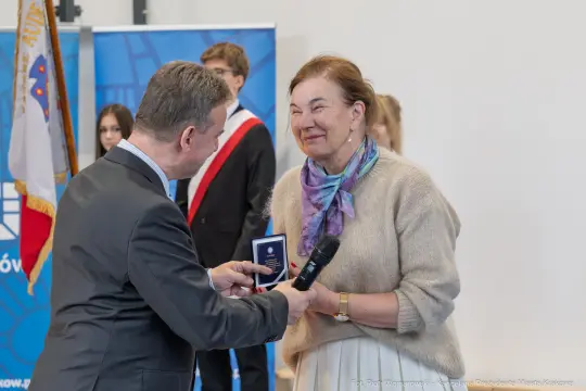Wręczenie odznaczenia przez mężczyznę kobiecie w eleganckim stroju.