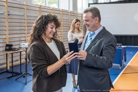 Wręczenie nagrody przez mężczyznę kobiecie w sali gimnastycznej.