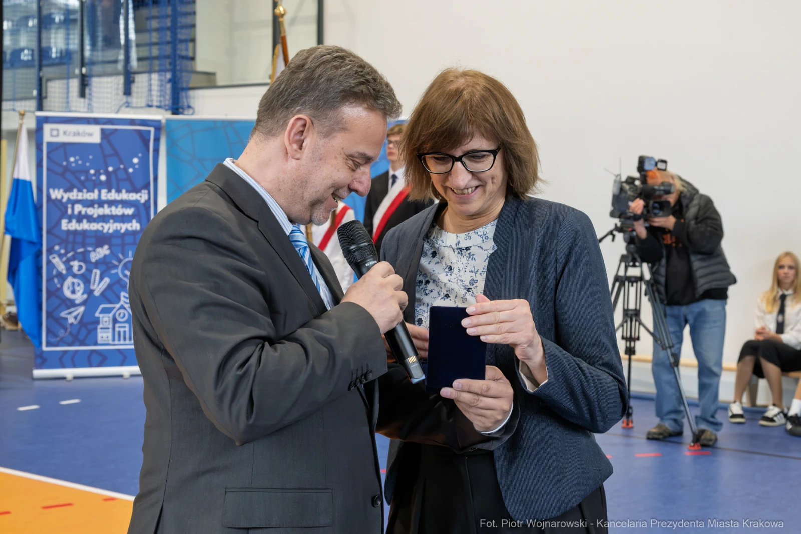 Mężczyzna i kobieta rozmawiają, trzymając telefon, w tle widoczni dziennikarze.  Autor: Piotr Wojnarowski